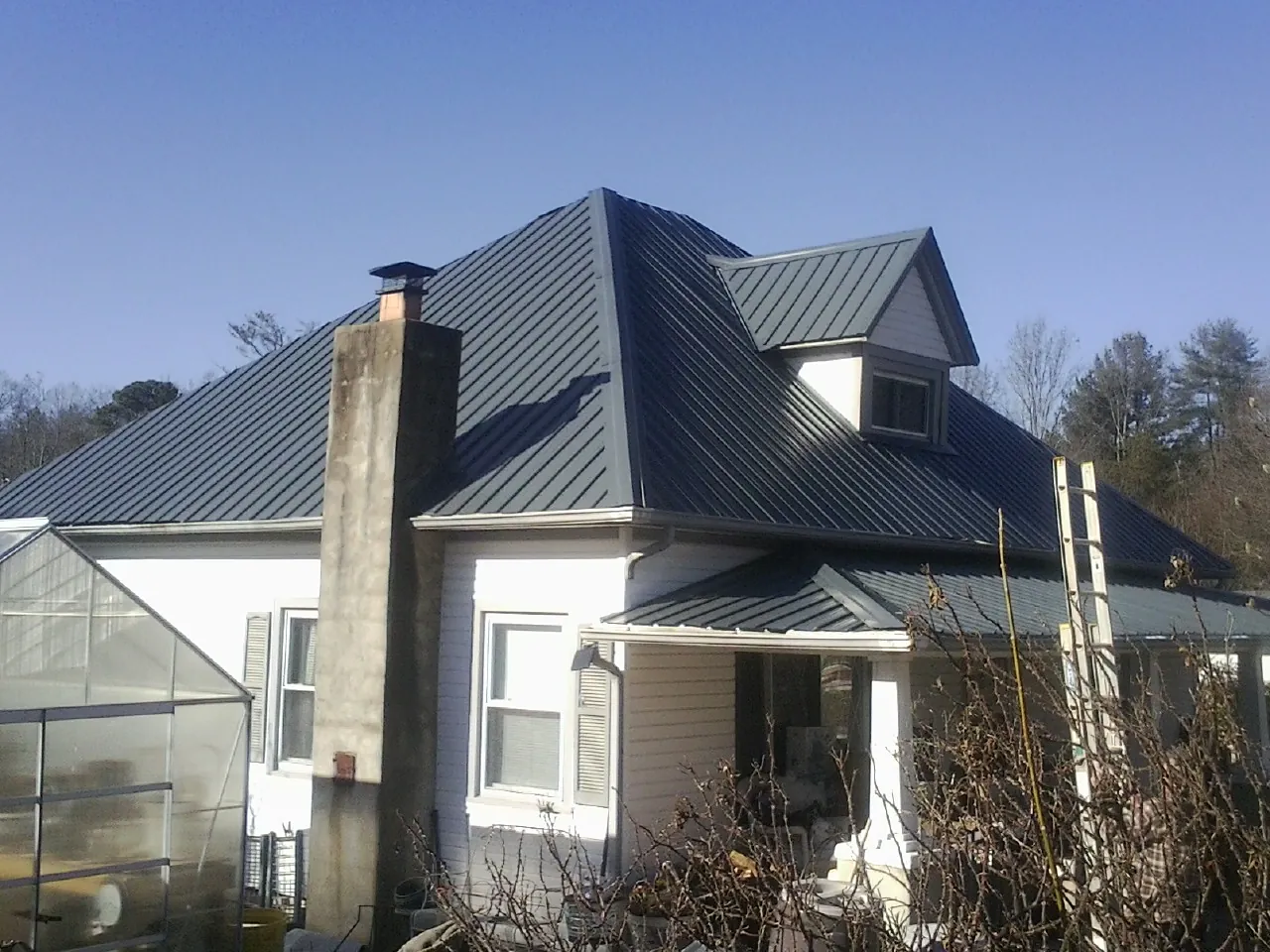 Dark blue standing seam metal roof on a white farmhouse with dormer — Slate & Tile Roof Repair by Roofing Brothers in Evart