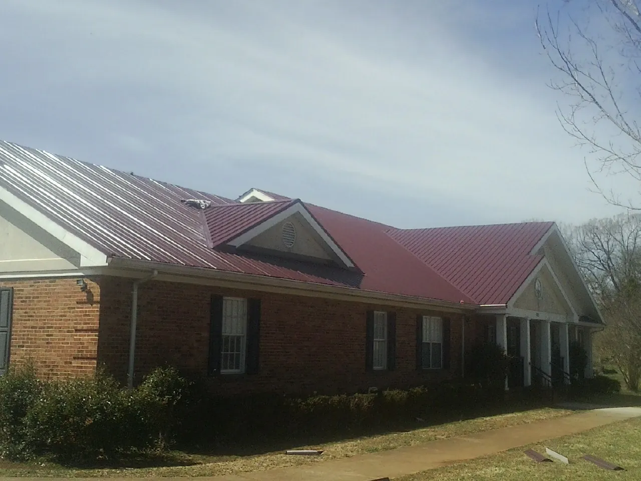 Red metal roof with gabled entries on a long brick building, from a Hail Damage Roof Repair job in Evart