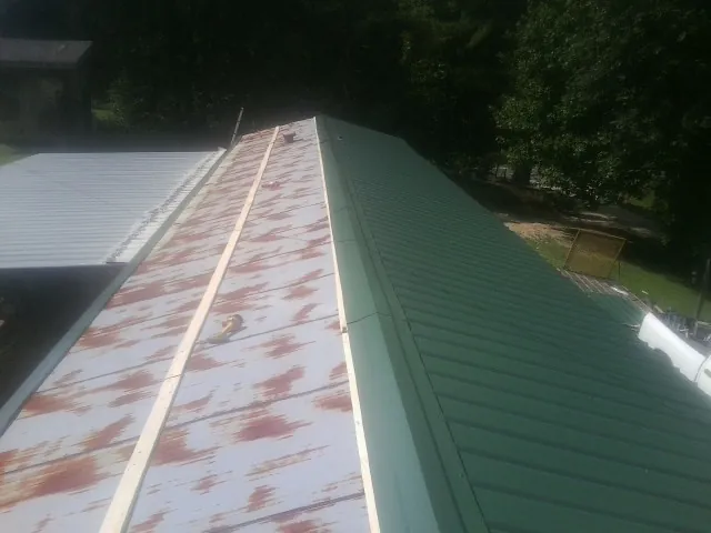 Old rusted panels beside newly installed green metal roofing — Wind Damage Roof Repair by Roofing Brothers in Evart