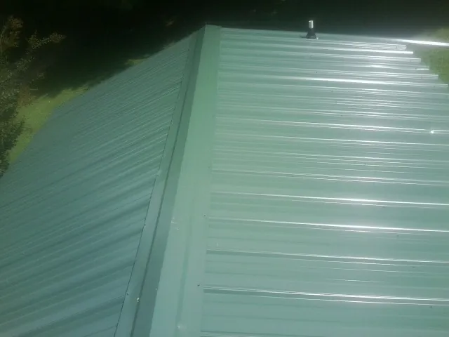 New green metal panels meeting at the ridge of a roof — Flat Roof Repair work by our crew in Evart