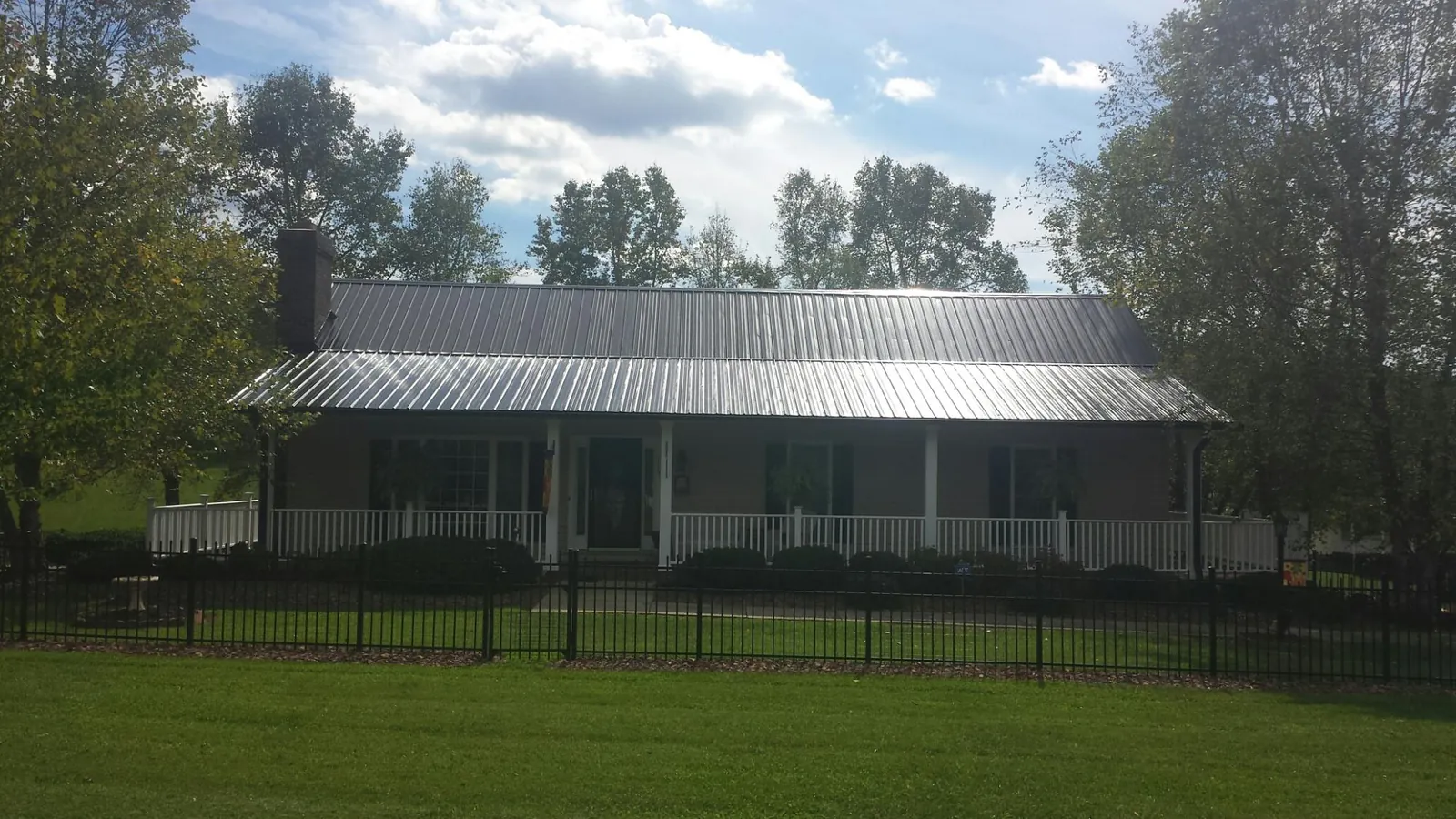 Gray metal roof on a brick ranch with a full width front porch — Gutter Guard Installation work by our crew in Evart