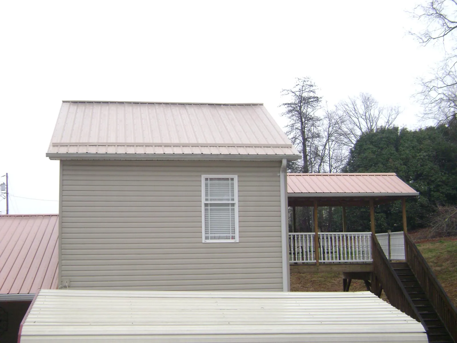 Tan metal roofs on a two story addition and attached porch, from a Roof Replacement job in Evart