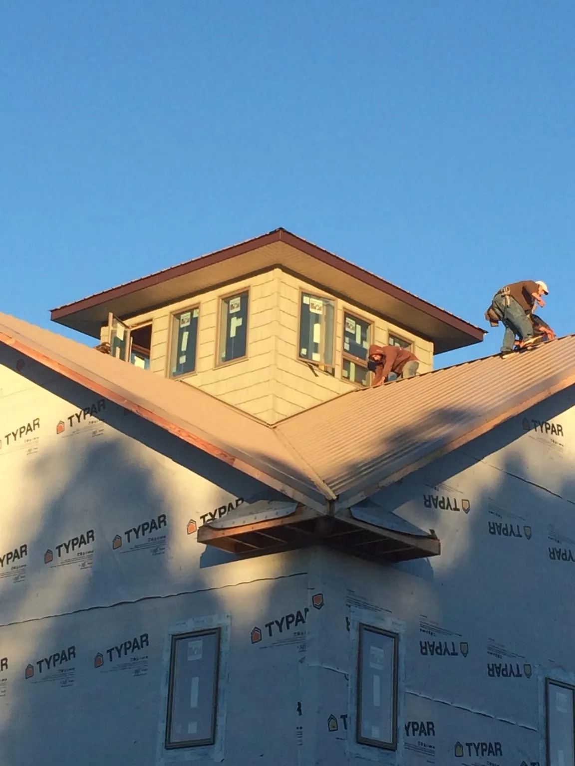Roofers working around a rooftop cupola on a new metal roof at sunset — Roof Waterproofing in Evart by Roofing Brothers